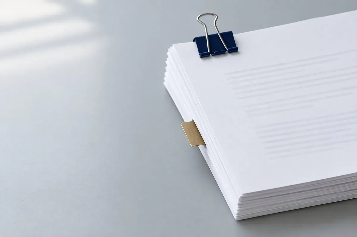A stack of blank printed pages held by a navy binder clip, with one gold tab marking a page