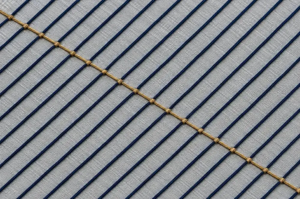 Navy threads running in parallel across pale linen, crossed and tied by a single gold thread